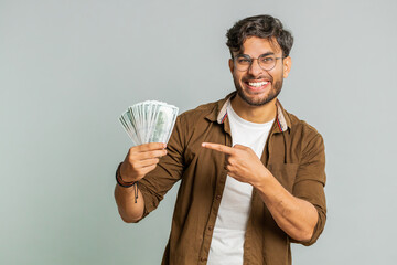 Rich pleased happy Indian young man waving money dollar cash banknotes bills like a fan, success...