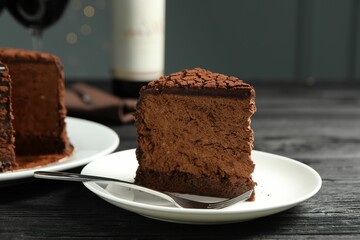 Piece of delicious chocolate truffle cake and fork on black wooden table, closeup