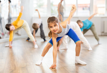 Fototapeta premium Group of focused tween children standing akimbo in row one by one, learning movements of folk dance in choreography lesson