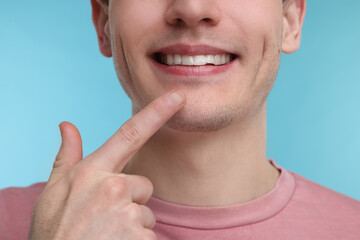 Young man showing his teeth with whitening strip on light blue background, closeup