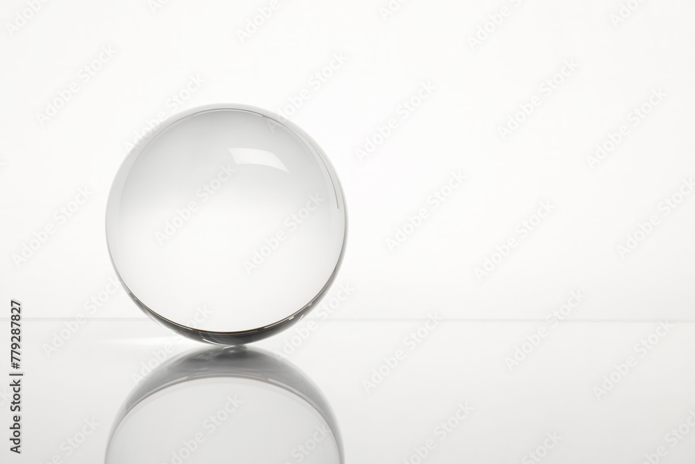 Sticker Transparent glass ball on mirror surface against white background. Space for text