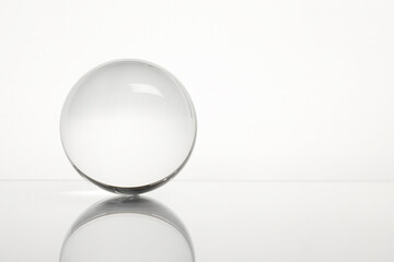 Transparent glass ball on mirror surface against white background. Space for text