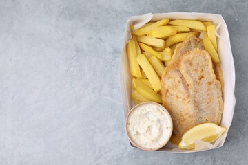 Delicious fish and chips with tasty sauce in paper box on gray table, top view. Space for text