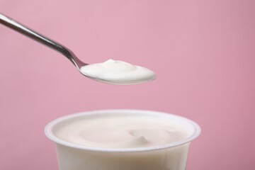 Eating delicious natural yogurt on pink background, closeup