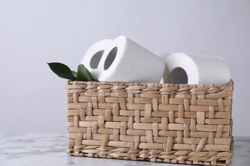 Toilet paper rolls and green leaves in wicker basket on white marble table