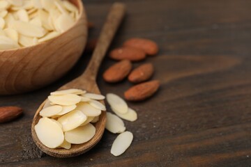 Fresh almond flakes and nuts on wooden table, closeup. Space for text