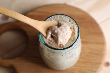 Taking sourdough starter with spoon at table, closeup