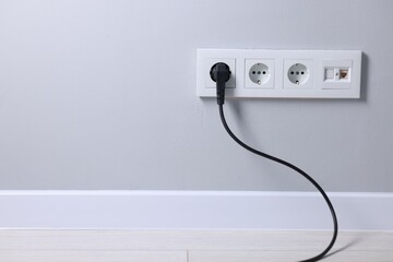 Power sockets and electric plug on grey wall, space for text