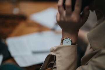 Close-up image of a business person in a beige blazer checking time on a gold wristwatch,...