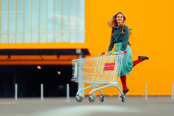Cheerful Shopper Jumping with Joy Pushing Shopping Cart. Excited woman feeling enthusiastic about...