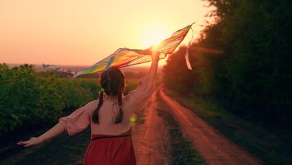 Happy girl runs along country road, plays with toy kite, sunset. Active Child runs with kite in...
