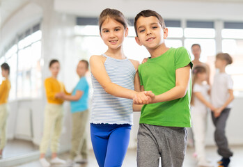 Joyous little boy and girl training waltz poses together with other attendees of dancing courses