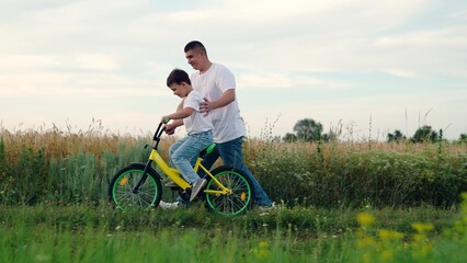 Childhood boy dream to ride bike. Dad teaches her little son to ride bicycle, sunset. Young father...