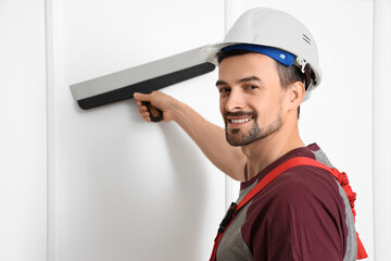 Male decorator with putty knife working in room