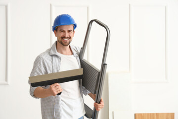 Male decorator with putty knife and stepladder in room