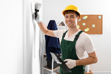 Male decorator with putty knives working in room