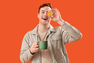 Young man with cup of tea and lemon on orange background