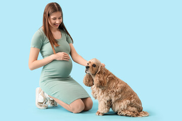Beautiful pregnant woman with cocker spaniel on blue background