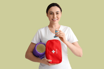 Sporty young woman with inhaler, first aid kit and foam roller on green background