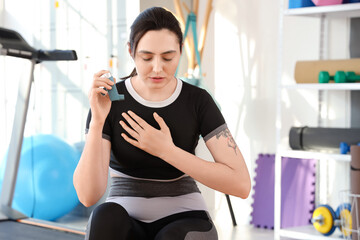 Sporty young woman with inhaler having asthma attack in gym