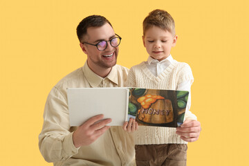 Happy father and his little son reading book together on yellow background