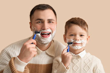 Happy father and his little son shaving on beige background