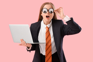 Young shocked businesswoman in funny disguise with laptop on pink background - obrazy, fototapety, plakaty
