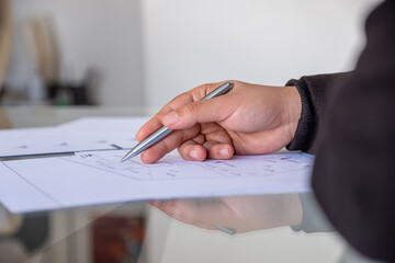 male holding pen while checking projects papers on glass table with reflections