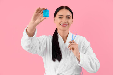 Beautiful young happy woman in bathrobe with dental floss and tongue scraper on pink background