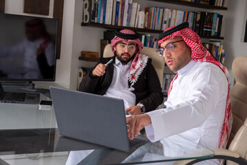arabic males working on project using laptop and papers while talking and checking all...