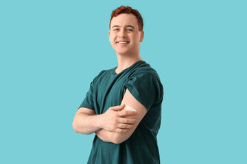 Happy young man with applied medical patch on blue background. Vaccination concept