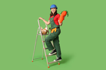 Happy female builder with Easter basket, toy carrot and ladder on green background