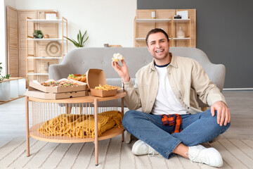 Young man in cream with unhealthy food on table at home. Overeating concept