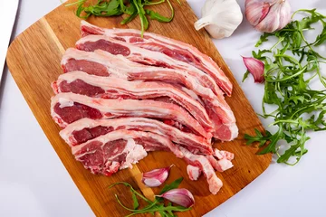 Foto op Plexiglas Raw lamb chops on wooden cutting board with garlic and herbs, over white background. © JackF