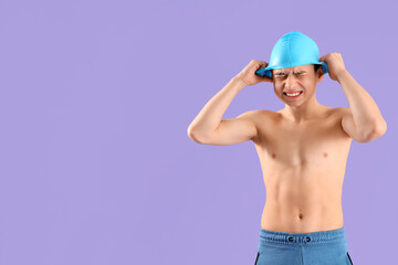 Angry little boy in swimming cap on purple background - obrazy, fototapety, plakaty