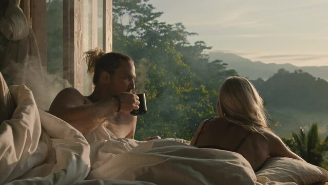 Lovers lying in bed with an amazing view and drinking coffee