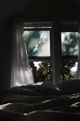 Open windows with curtains billowing in a summer breeze with an unmade bed in the foreground.