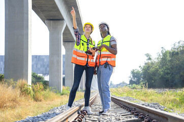 multi ethnic railway construction workers working outdoors,standing at rail tracks,discuss work,african woman technician having walkie talkie and blue print,caucasian female holding digital tablet - obrazy, fototapety, plakaty