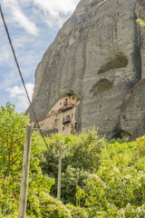 A secluded monastery embedded in a sheer rock face amidst vibrant green foliage in Meteora, Greece