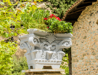 Ornate white classical planter with red flowers in front of a textured stone wall in Meteora, Greece