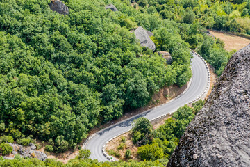 Aerial view of a serpentine road weaving through foliage and around steep cliffs in Meteora, Greece