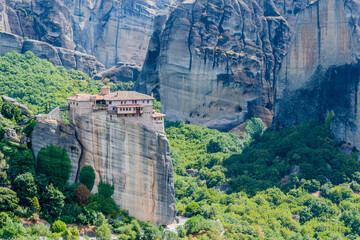 A historic monastery sits atop a sheer cliff amidst green foliage in Meteora, Greece