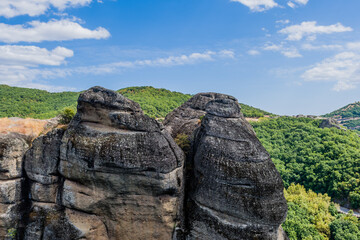 Majestic rock formations with dark crevices amidst green vegetation under a clear blue sky in Meteora, Greece