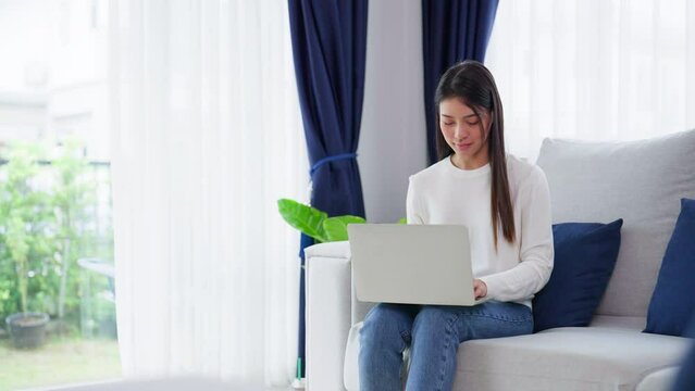 Young asian woman using laptop while seated on couch at home