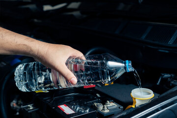 The mechanic fills the car's windshield wiper tank with water and inspects the engine before...