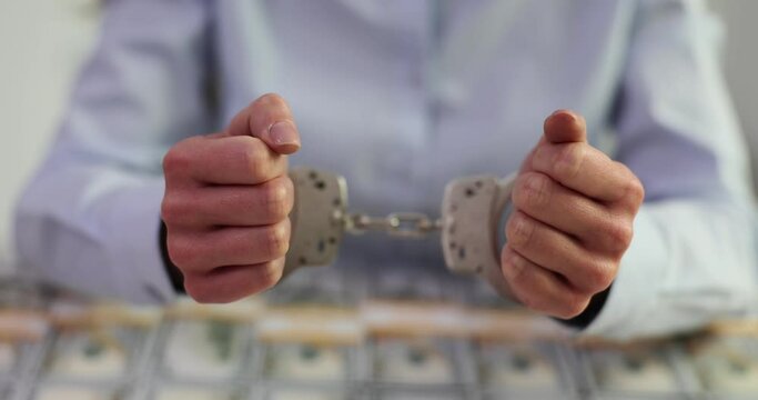 Hands of a corrupt female politician official in handcuffs and US dollars