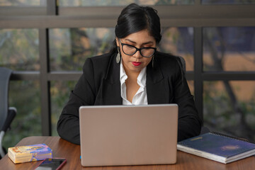 Serious woman with glasses working on her laptop inside her work office