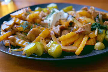 Fried potatoes with mushrooms, onion, meat, pickles on the plate