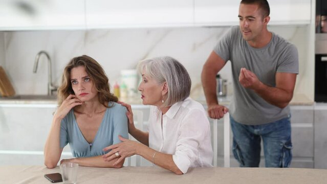 Adult man during family quarrel with elderly woman and adult woman in kitchen