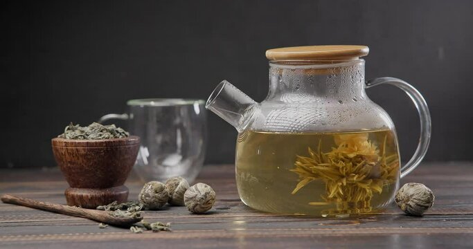 Blooming flower tea ball brewing in a glass teapot with Hot boiling water on wooden background
